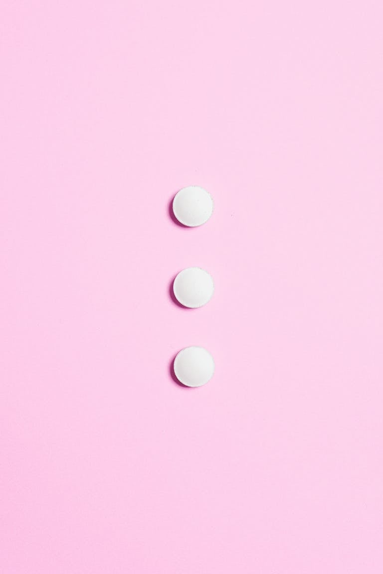 A minimalist composition featuring three white pills on a vibrant pink background.