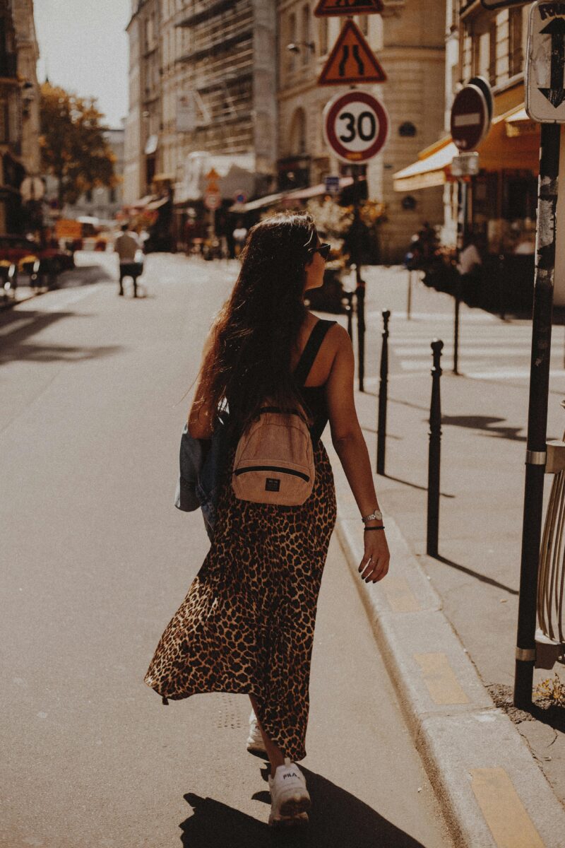 Woman in leopard skirt walking down a sunlit street in Paris, capturing urban charm.