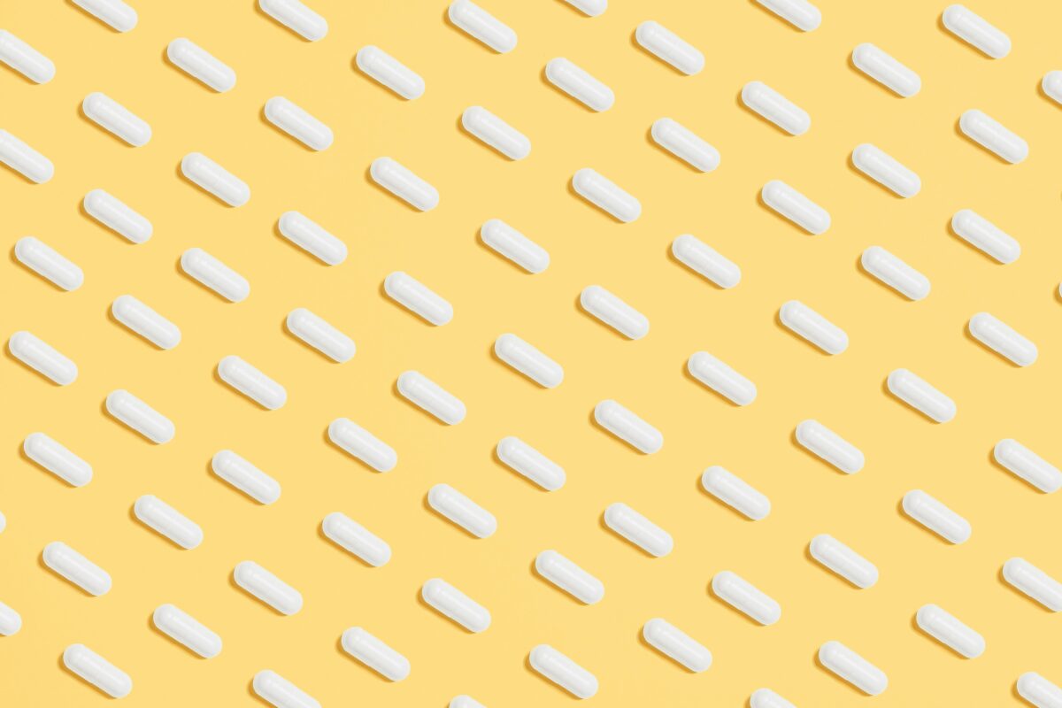 Pattern of white capsules on a bright yellow surface, symbolizing healthcare and medicine.