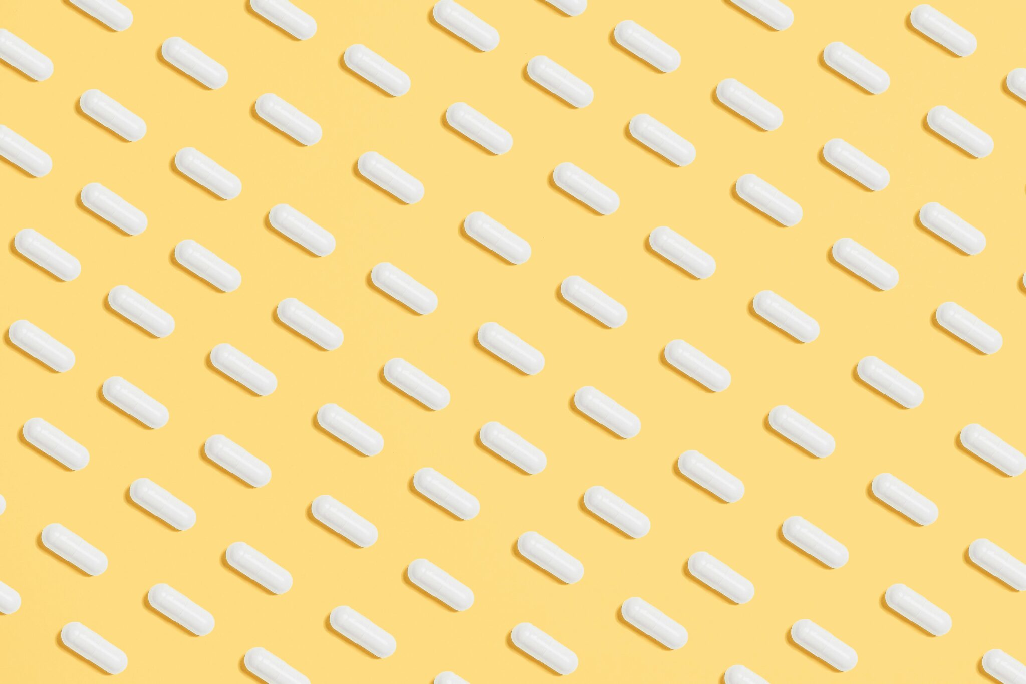 Pattern of white capsules on a bright yellow surface, symbolizing healthcare and medicine.