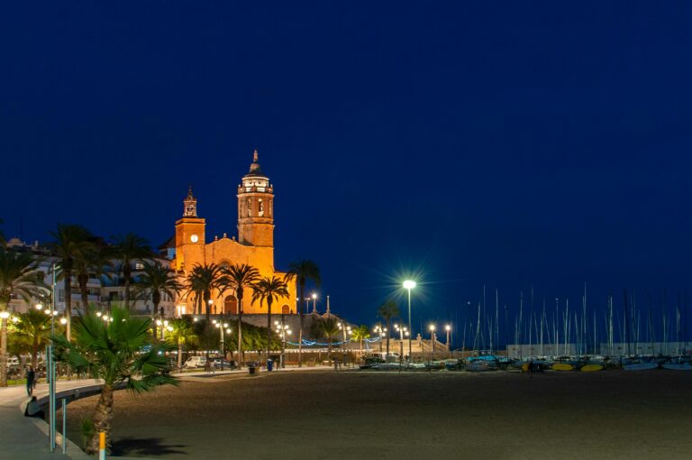 Capture of the illuminated church and promenade by the beach in Sitges, Spain at night.